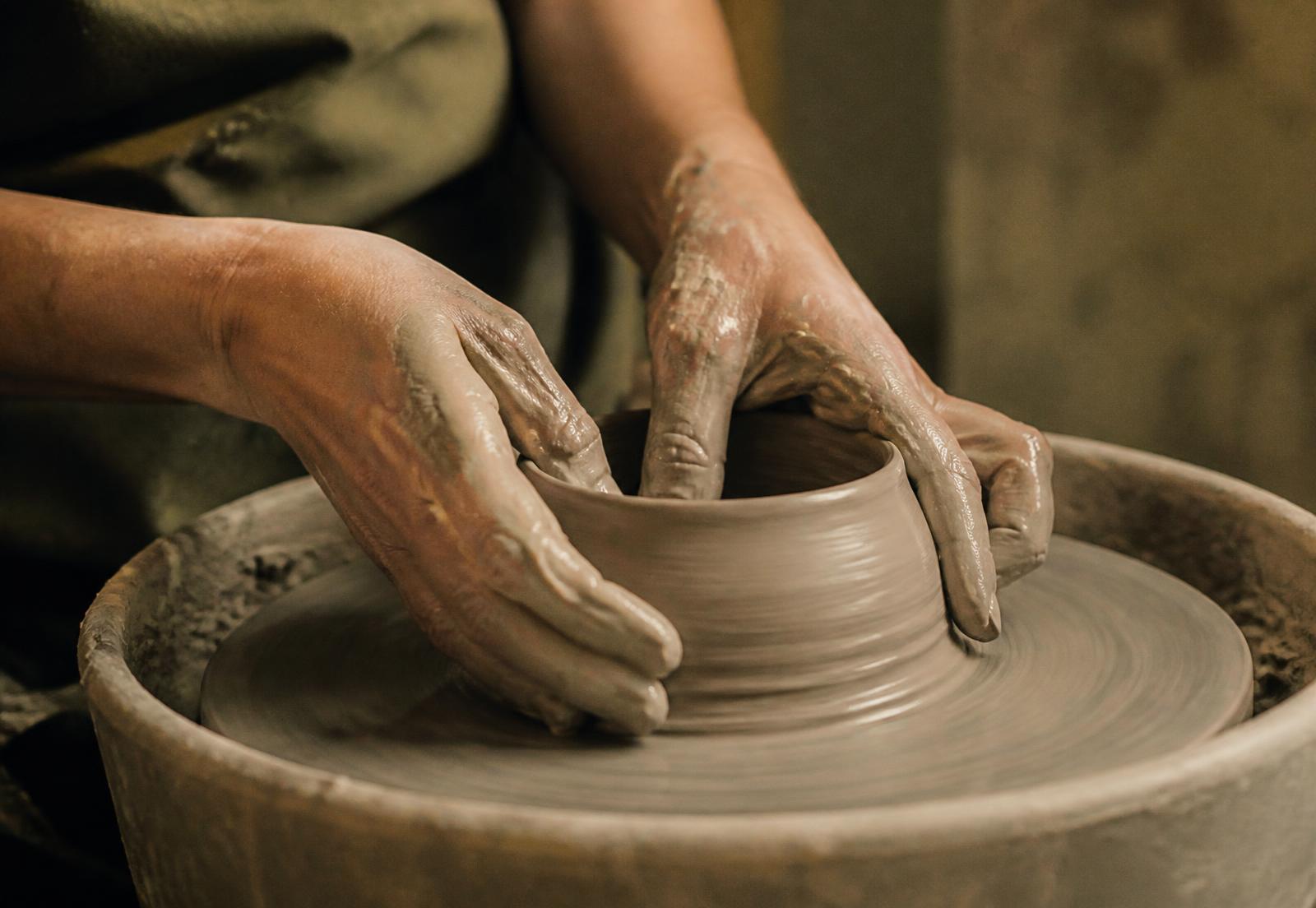 Two hands shaping a bowl of wet clay on a potter's wheel